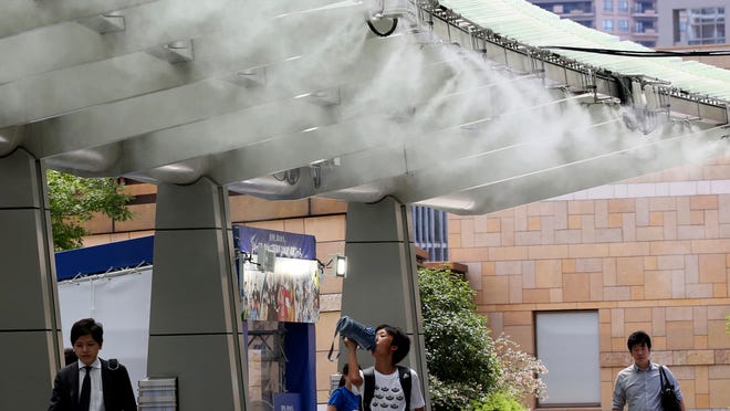People chill under a cooling mist spot in Tokyo on July 23, 2018. Searing hot temperatures are forecast for wide swaths of Japan and South Korea in a long-running heat wave.