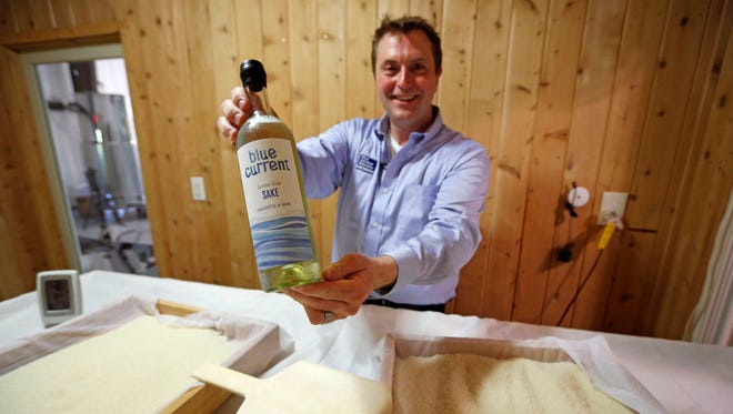 In this photo taken, Friday, June 12, 2015, Dan Ford, founder of the Blue Current Brewery, poses with a bottle of sake at the brewery in Kittery, Maine.