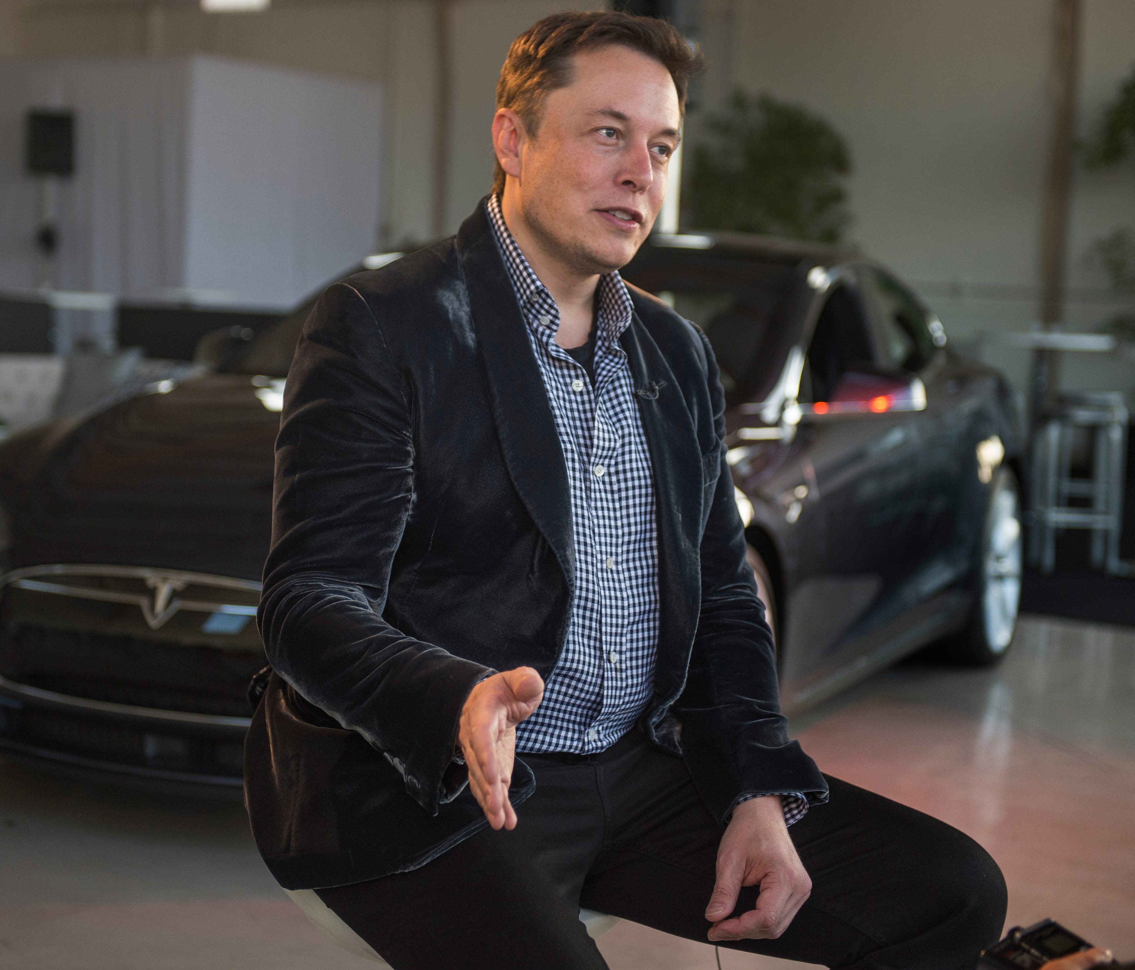 Elon Musk, Tesla CEO, discusses new technologies that before an event for Tesla owners and the media held at the Hawthorne Airport on Oct. 9, 2014. In the background is a Tesla model P85D.