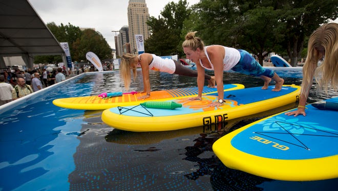 Julie DeVoe, left, Amelia Travis, middle, and Jaysea DeVoe demonstrate yoga on a Glide brand paddle board in a demo pool at the Outdoor Retailer Show on Wednesday, Aug. 5, 2015, in Salt Lake City.  In the last few years there has been significant growth in the popularity of paddle boarding.