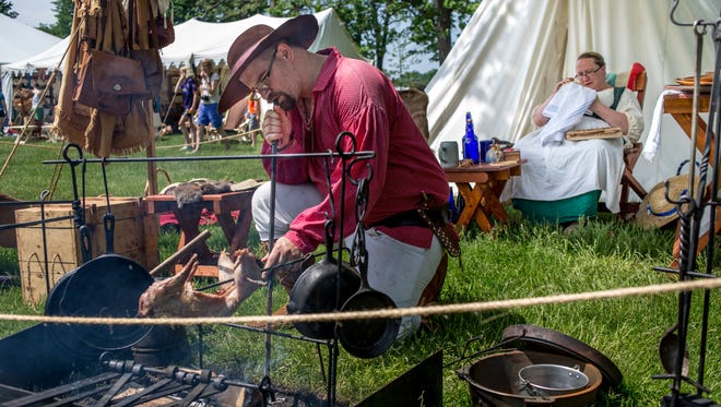 Joe Fackler, of New Baltimore, stokes a fire while he cooks a whole rabbit as his wife, Amanda Fackler, works on cross stitching during the Feast of the Ste. Claire Saturday, May 28, 2016 at Pine Grove Park in Port Huron.