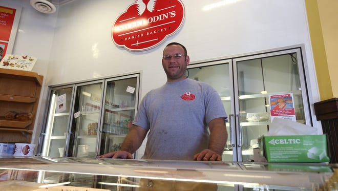 Kevin Olesen, owner of Sweet Odin’s Danish Bakery, stands in front of specialty-made cakes and pastries in his store.