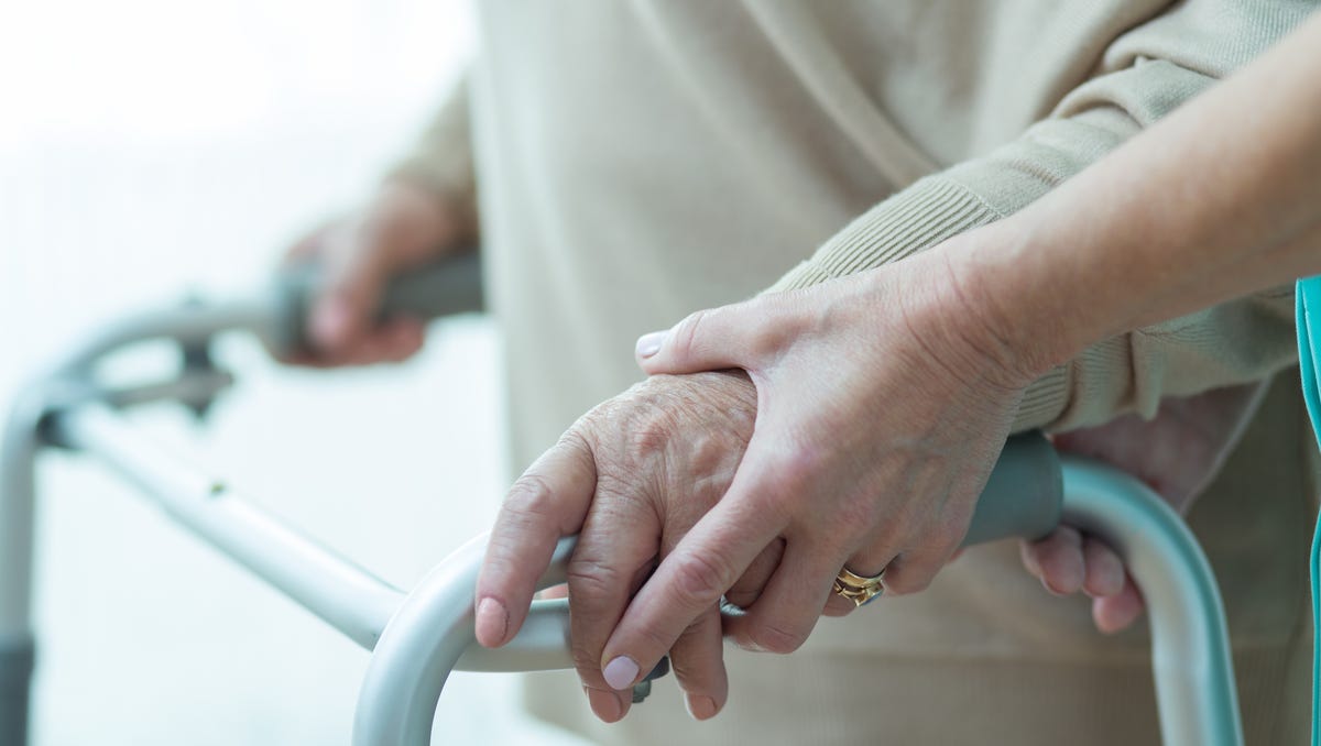 A woman using a walker is assisted by a caregiver.