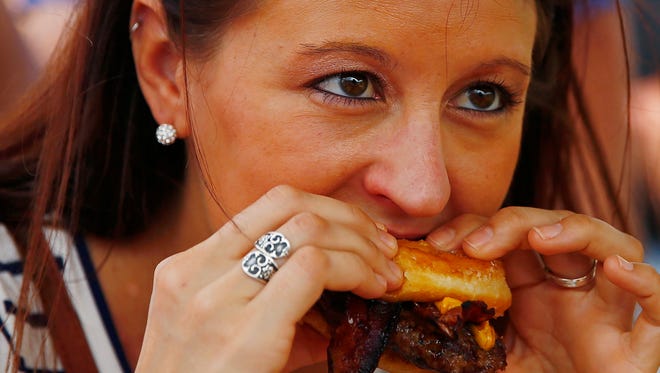 Shanta Johnson bites down on a donut burger Saturday, Nov. 14, 2015 at the Naples Municipal Airport. A few thousand people enjoyed the second annual Baconfest to raise money for hungry children in Southwest Florida. Hosted by the Kiwanis Club of Pelican Bay, the event featured dozens of food and beverage vendors, bacon-eating contests, raffles, the music of five bands, a play area for youngsters, animals and more. (Corey Perrine/Staff)