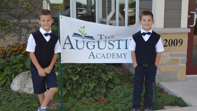 Two students of The Augustine Academy stand by a sign promoting the school, which opened in fall 2016 at First Baptist Church in the village of Merton.
