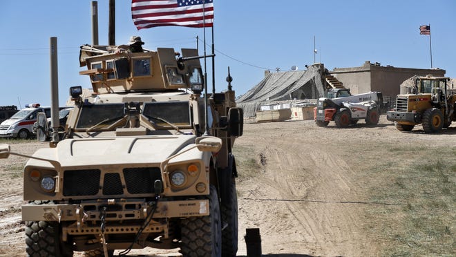 In this April 4, 2018 file photo, a U.S. soldier, left, sits on an armored vehicle behind a sand barrier at a newly installed position near the front line between the U.S-backed Syrian Manbij Military Council and the Turkish-backed fighters, in Manbij, north Syria. An American military official said on Jan. 11, 2019, that the U.S.-led military coalition has begun the process of withdrawing troops from Syria.