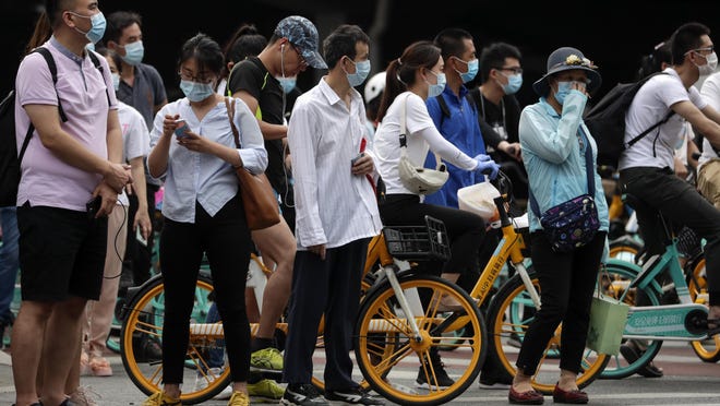 People wearing protective face masks to help curb the spread of the new coronavirus wait to cross a street in Beijing, Monday, June 22, 2020. A Beijing government spokesperson said the city has contained the momentum of a recent coronavirus outbreak that has infected a few hundreds of people, after the number of daily new cases fell to single digits.