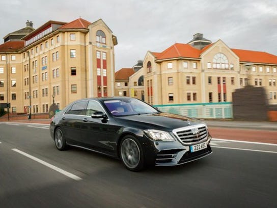 The Mercedes-Benz S Class Salon in the color black is shown speeding on a road with buildings in the background.