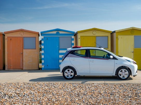 A white Toyota Aygo x-claim exterior pictured in front of colorful sheds on a beach