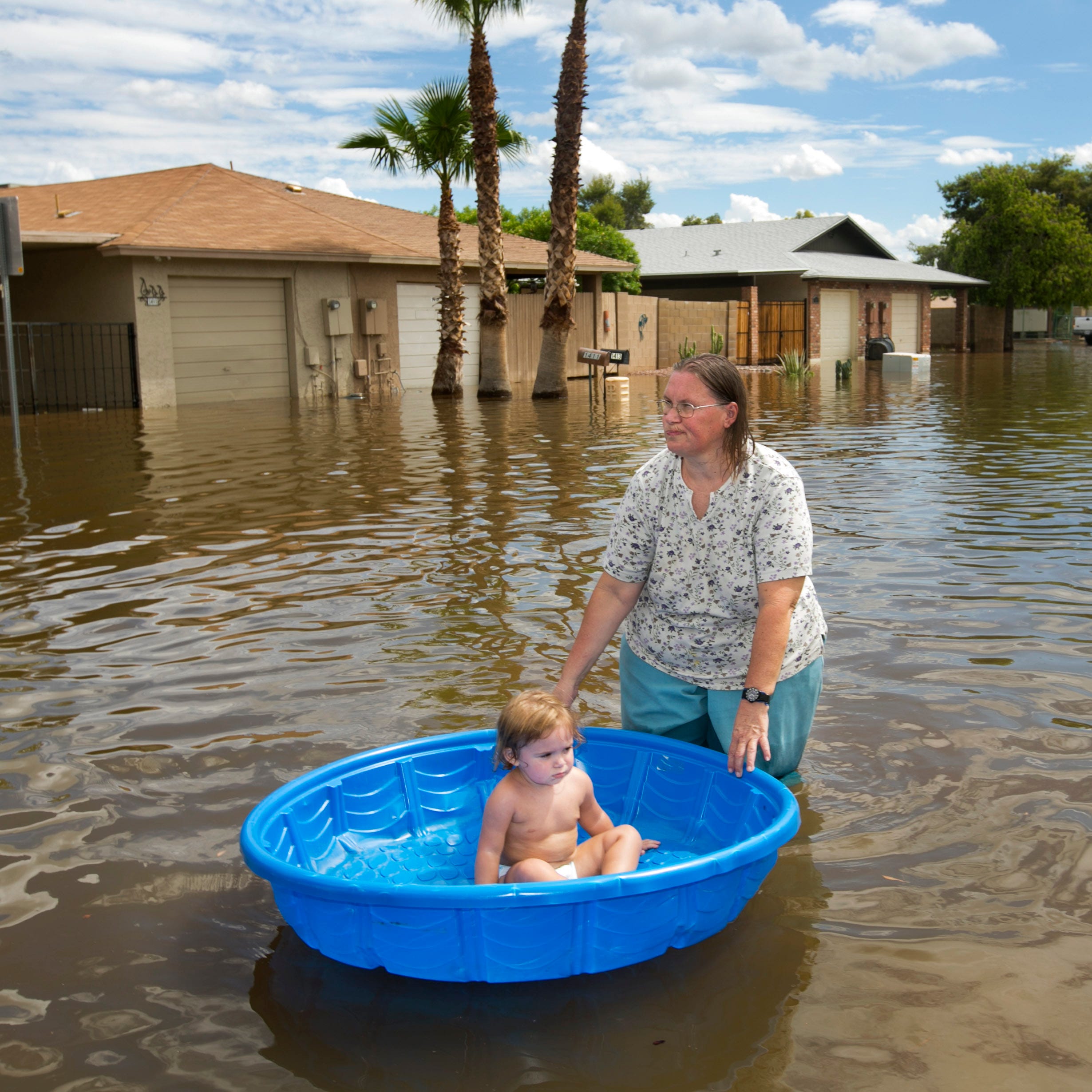 Laura Moravek carries her granddaughter, Alyssa Guarino, in a pool as they walk through the flooded road of South Allen, just east of Stapley Drive in Mesa on Tuesday, September 9, 2014.