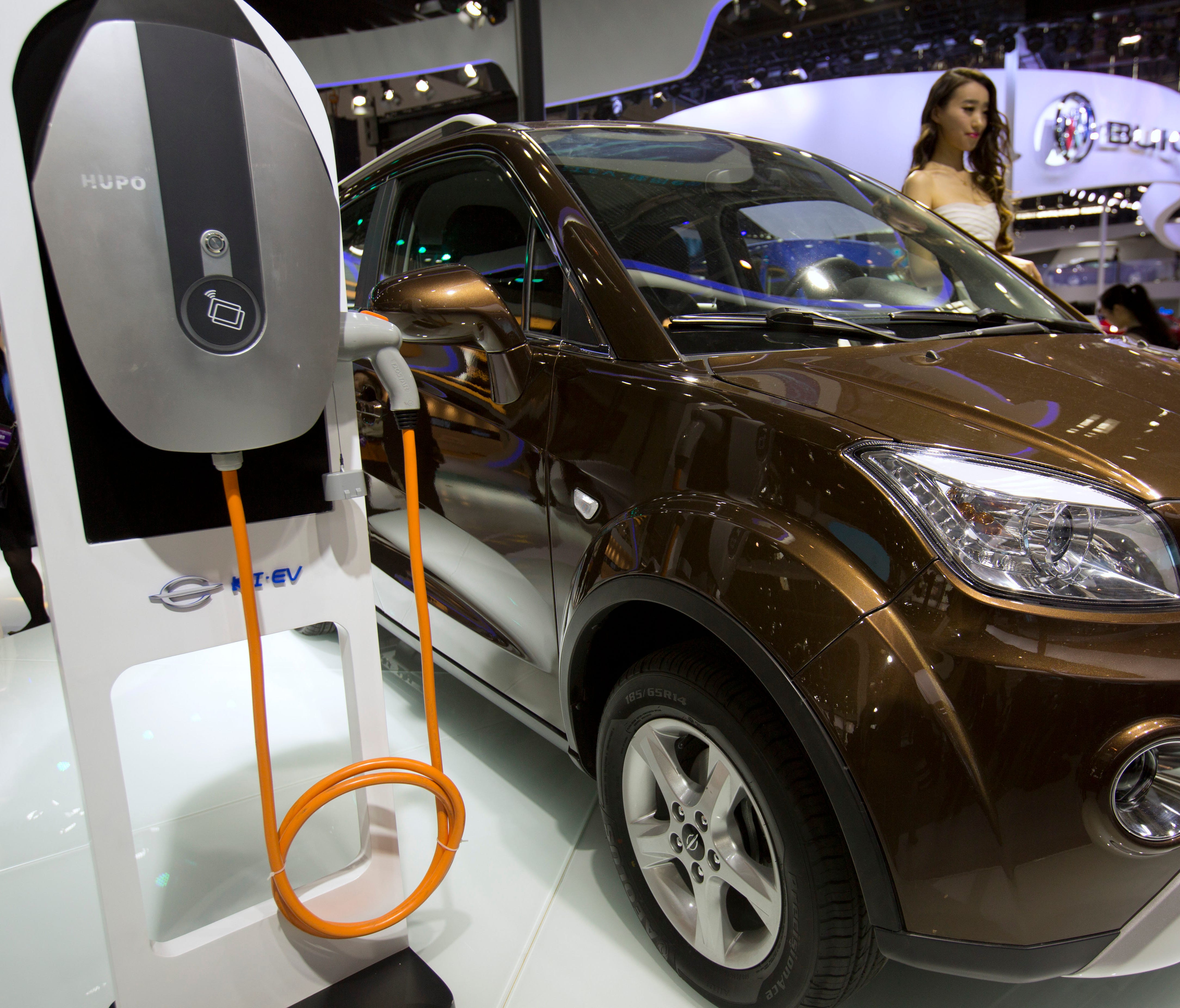 FILE - In this April 26, 2016, file photo, a staff member stands next to an e.Cool electric SUV by Chinese automaker Changjiang on display at the Beijing International Automotive Exhibition in Beijing. China has stepped up pressure on automakers to a