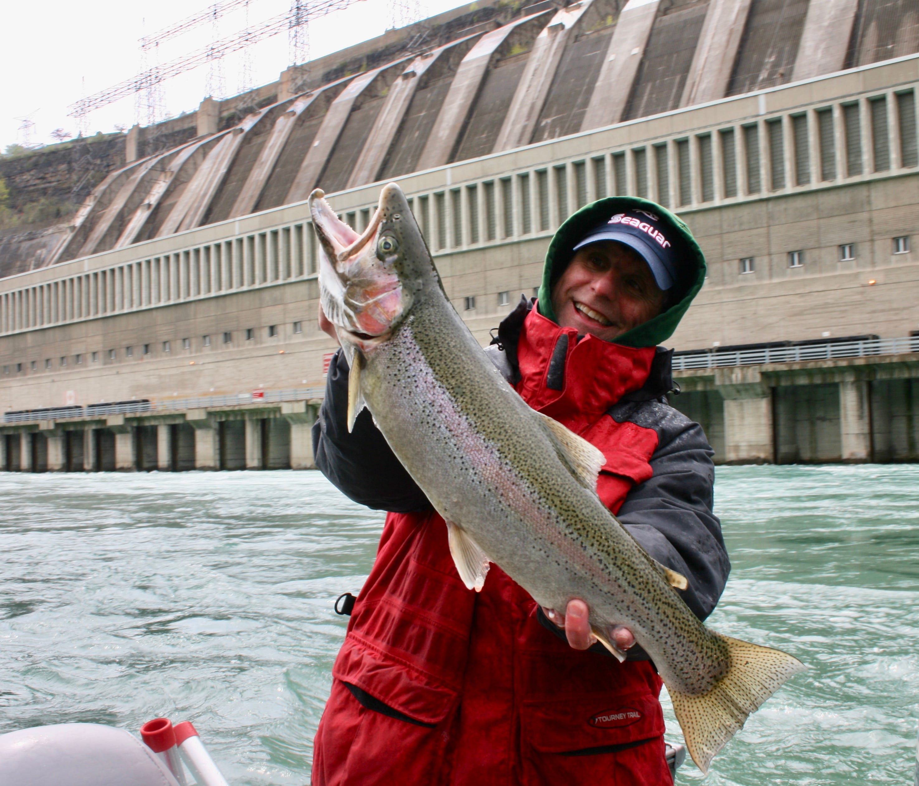 Capt. Joe Marra with a Niagara River steelhead. Water released from the Niagara Hydroelectric Power Station (seen in the background) adds to the swirling currents that challenge boaters.