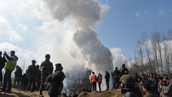 Indian soldiers and Kashmiri onlookers stand near the remains of an Indian Air Force helicopter after it crashed in Budgam district, outside Srinagar on Feb. 27, 2019.