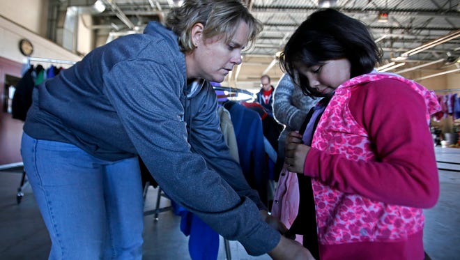 At left, volunteer Jenny Baker helps Wendy Vidales, 7, try on a hooded sweatshirt during the Coats for Kids distribution event on Saturday at  Farmington Fire Station No. 6.