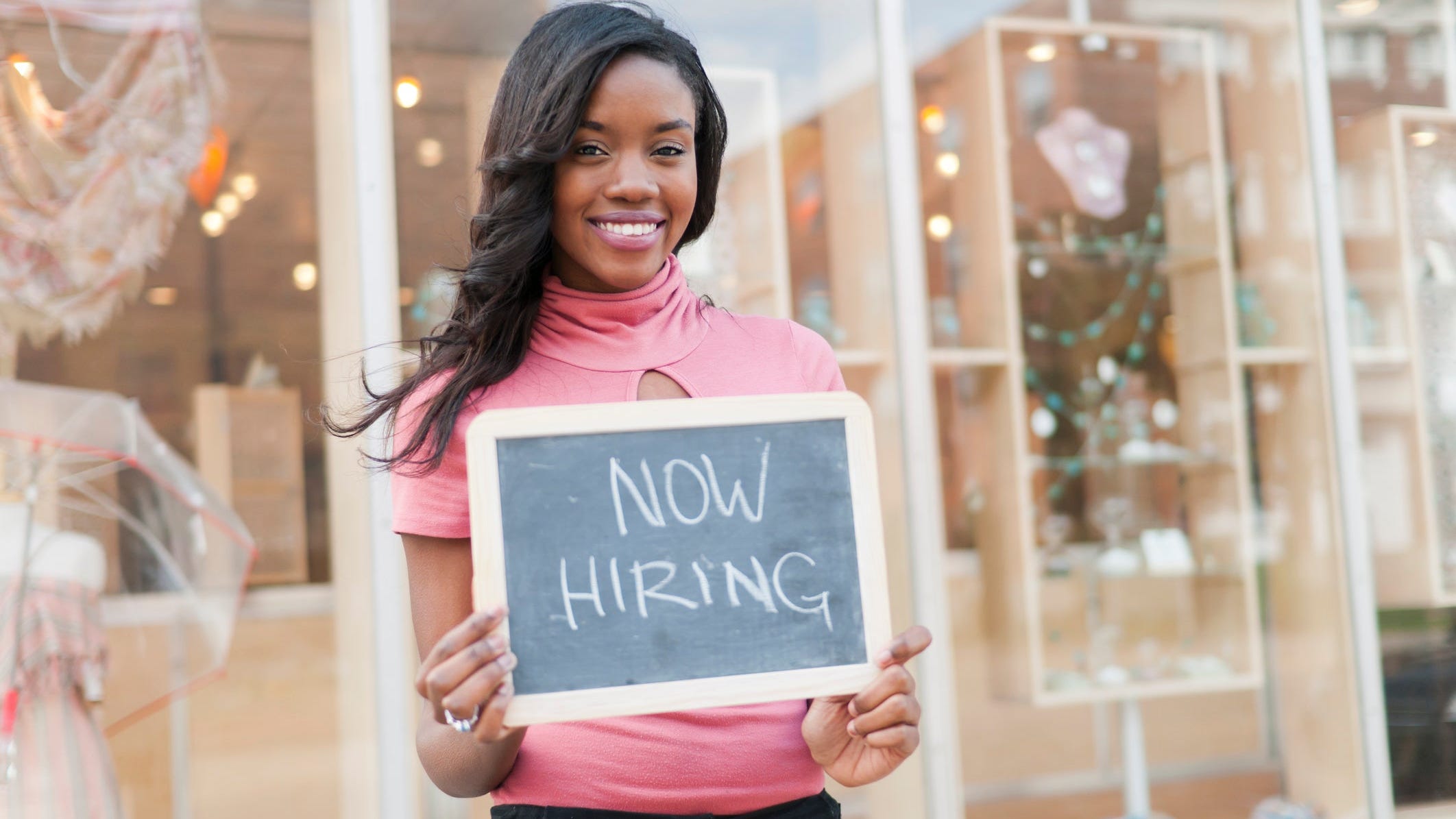 A woman holding up a now hiring sign.
