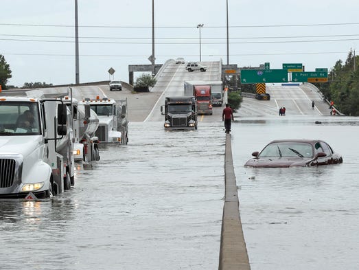 A man walks down the median as trucks navigate floodwaters