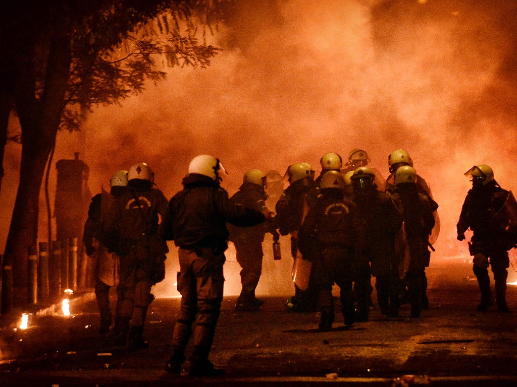 Police officers stand amid tear gas and smoke from Molotov cocktails in the central district of Exarchia in Athens Greece at the end of a demonstration to mark the eighth anniversary of a teenager's death at the hands of police in 2008. Hooded youths