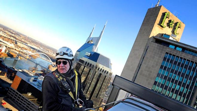 Above, Jim Webster hangs over the edge of the ServiceSource building at Fourth Avenue and Church Street as he prepares to rappel to change a sign. Below, he helps guide down letters that he and his team are changing 20 stories up.