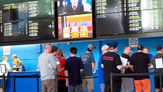 FILE - In this June 19, 2018, file photo, sports bettors line up at windows at Monmouth Park racetrack in Oceanport, N.J. With the legalization of sports gambling in the United States and its gradually expanding implantation, some in the industry are suggesting horse racing add fixed-odds wagering as a way to respond to the changing landscape, evolve and compete with the other options now available. (AP Photo/Wayne Parry, File)