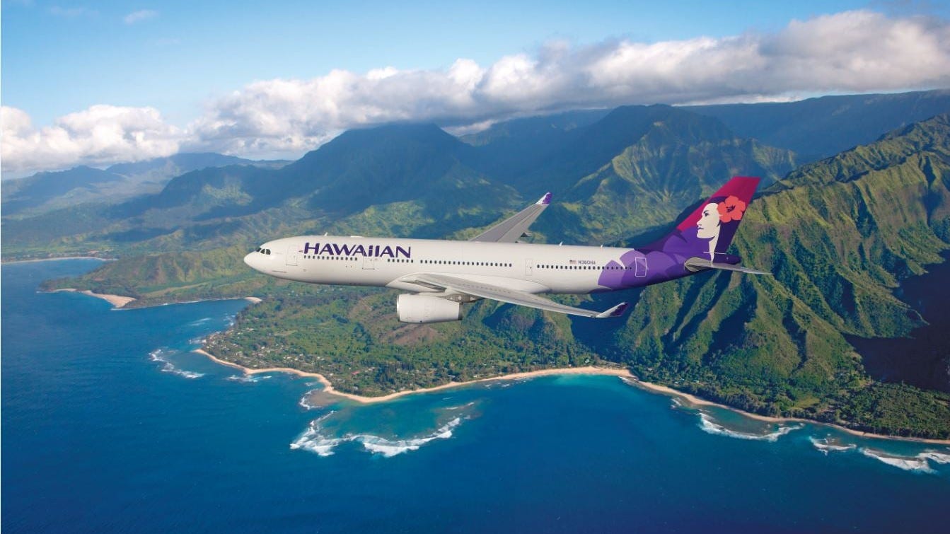 A Hawaiian Airlines plane flying over the ocean, with mountains in the background