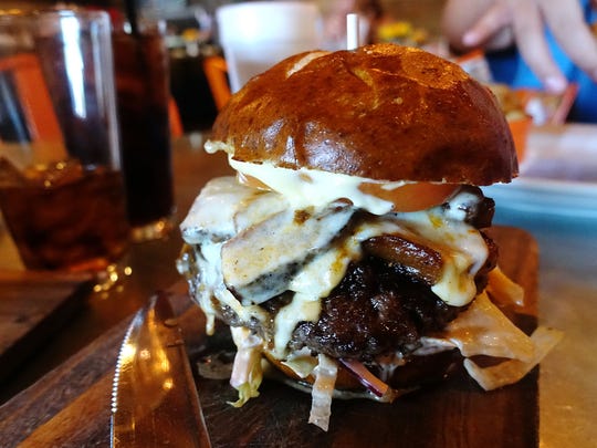 Bootlegger burger with muenster cheese, whiskey onions, confit slab bacon, lettuce, tomato, red onion, dijonnaise, house sauce and pretzel bun at Bootleggers Modern American Smokehouse in Scottsdale, AZ.