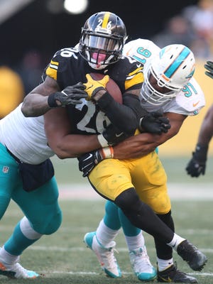 Pittsburgh Steelers running back Le'Veon Bell (26) runs the ball against Miami Dolphins defensive tackle Ndamukong Suh (left) and defensive end Cameron Wake (91) during the third quarter in the AFC Wild Card playoff football game at Heinz Field. The Steelers won 30-12.