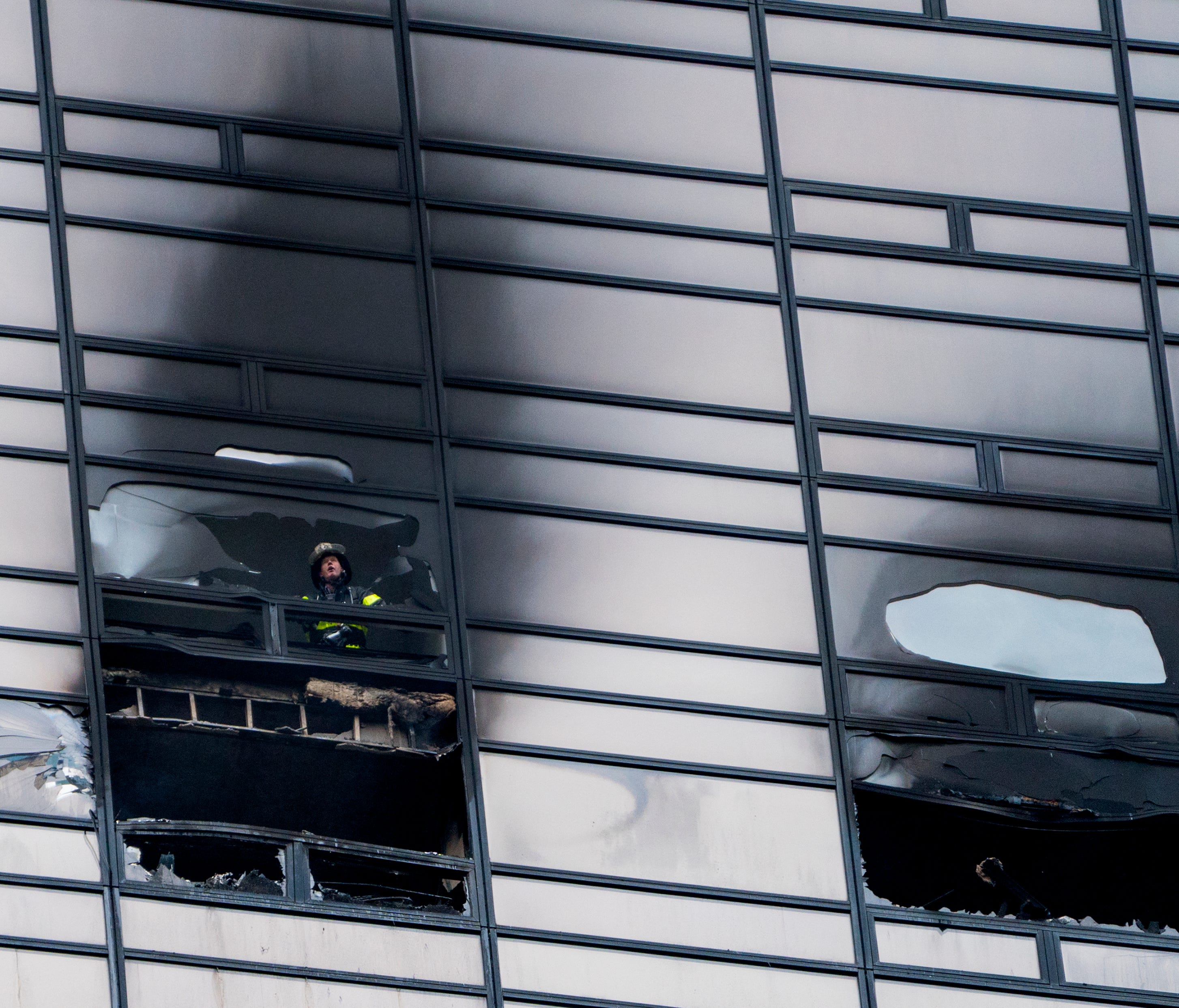 A firefighter looks out from the window of a damaged apartment in Trump Tower in New York on Saturday, April 7, 2018.