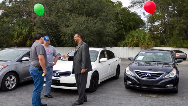 Brothers Arturo Alarcon and Ignacio Alarcon talks with salesman Carlos Garay about a car at Grant Motors in Fort Myers on Friday.