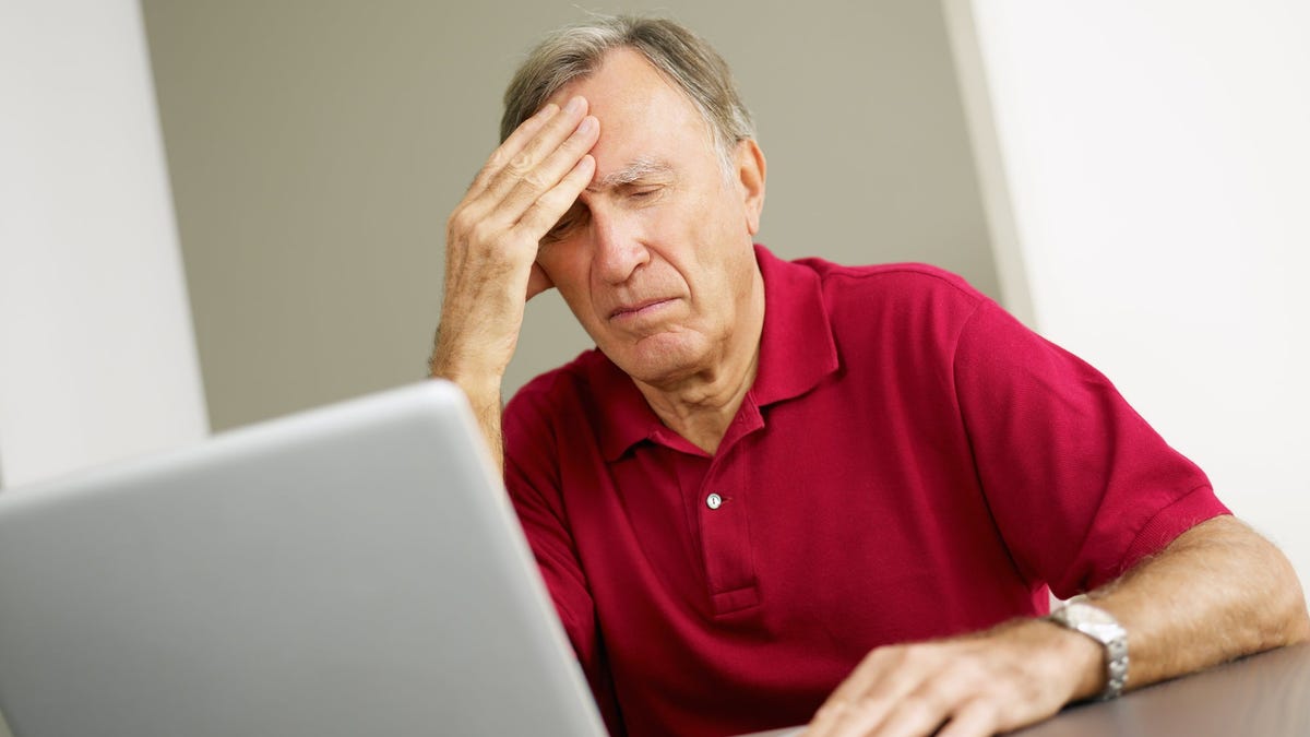Older man at laptop with distressed expression holding his head