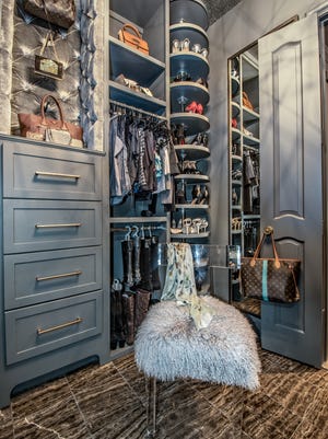 Custom "hers" closet with velvet tufted insets, a shoe carousel and pull down racks. The fluffy chair, marble flooring and lighting accents give it a boutique feel.