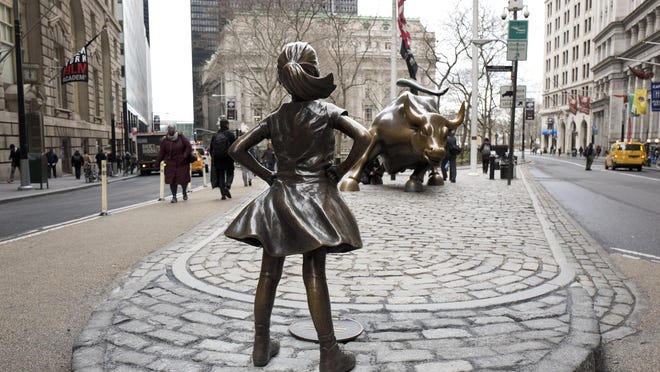 In this March 8, 2017, the "Fearless Girl" statue faces Wall Street's charging bull statue in New York. It took months of intricate planning by two corporate giants to install the statue under the veil of darkness in time for Wednesday's International Women's Day. The one-week permit for the installation downtown was extended by New York Mayor Bill de Blasio through April 2 and popular support for the piece to be kept permanently is growing, with petitions being signed. (AP Photo/Mark Lennihan)