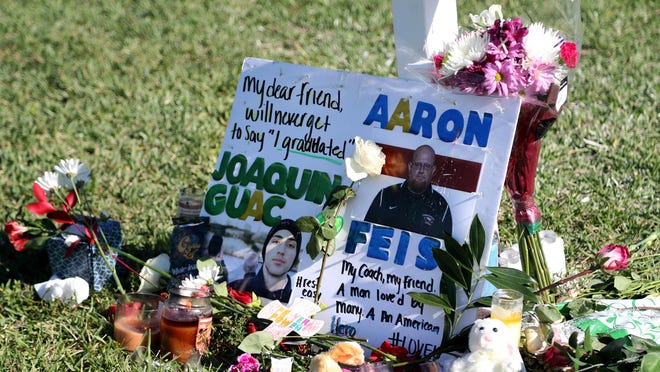 A tribute to student Joaquin Oliver and Coach Aaron Feis is left at the base of a white cross at Pine Trails Park in Parkland, Fla., on Friday, Feb. 16, 2018. White crosses stand in a field at the park to memorialize the 17 people killed Wednesday at Marjory Stoneman Douglas High School. (Amy Beth Bennett/Sun Sentinel/TNS)