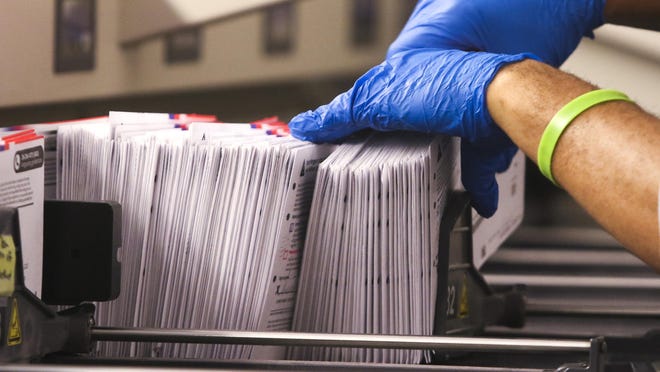 An election worker handles vote-by-mail ballots coming out of a sorting machine for the presidential primary at King County Elections in Renton, Wash., on March 10.