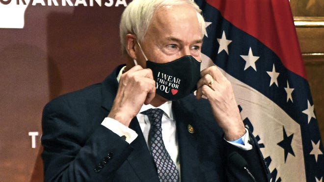 Gov. Asa Hutchinson removes his mask before a briefing at the state Capitol.