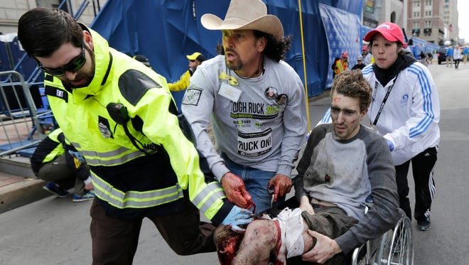 In this Monday, April 15, 2013, file photo, Boston EMT Paul Mitchell, left, bystander Carlos Arredondo, in cowboy hat, and Boston University student Devin Wang push Jeff Bauman in a wheelchair after he was injured in one of two explosions near the finish line of the Boston Marathon. Bauman and his three rescuers, became one of the most recognizable and powerful symbols of Boston's resilience after the April 15 attacks.