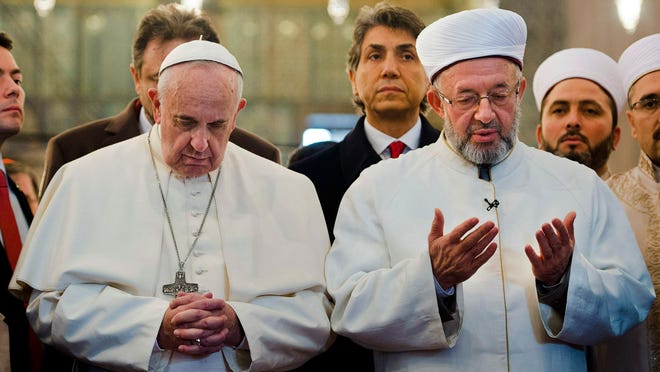 In this photo provided by Vatican newspaper L'Osservatore Romano, Pope Francis joins Grand Mufti of Istanbul, Rahmi Yaran praying in the Sultan Ahmet mosque in Istanbul, Turkey, Saturday, Nov. 29, 2014. Meeting with Turkish leaders in the capital Ankara a day earlier, Francis urged Muslim leaders to condemn the "barbaric violence" being committed in Islam's name against religious minorities in Iraq and Syria.