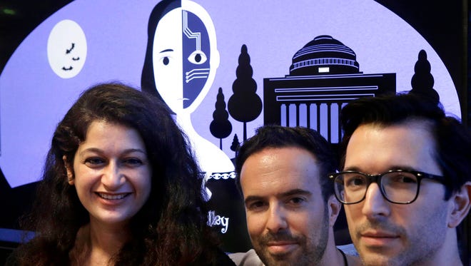 Creators of a fiction-writing "chatbot," from the left, Massachusetts Institute of Technology postdoctoral associate Pinar Yanardag, of Istanbul, Turkey; MIT research scientist Manuel Cebrian, of Madrid, Spain; and MIT associate professor Iyad Rahwan, of Aleppo, Syria; sit for a photograph in front of a graphic from the home page of the site called "Shelley." Named after "Frankenstein" author Mary Shelley, the chatbot has been trained on more than 140,000 horror stories written by amateur writers on a popular online forum. Now Shelley is generating its own stories on Twitter, taking turns with humans in an experiment to find out if artificial intelligence is smart enough to make someone feel scared.