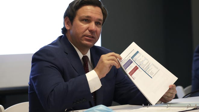 Florida Gov. Ron DeSantis holds up a document pertaining to COVID-19 during a news conference at the old Pan American Hospital on Tuesday in Miami.