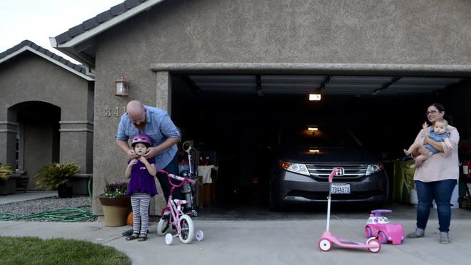 Enterprise football coach Russell McWilliams (left) puts a bike helmet on his daughter Rachel, 4, while his wife Vanessa holds their daughter Sophia, 6 months, at their home in Anderson.