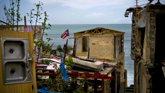In this Oct. 5, 2017 file photo, a Puerto Rican national flag is mounted on debris of a damaged home in the aftermath of Hurricane Maria in the seaside slum La Perla, San Juan, Puerto Rico. An independent investigation ordered by Puerto Rico’s government estimates that nearly 3,000 people died as a result of Hurricane Maria.