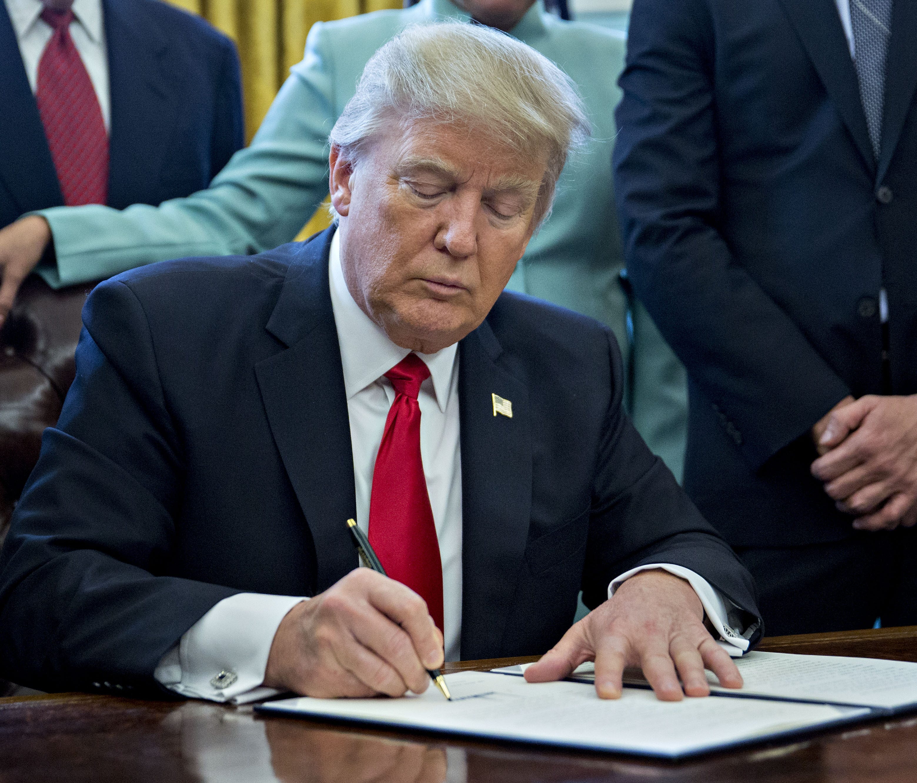 President Donald Trump signs an executive order in the Oval Office of the White House surrounded by small business leaders Monday.