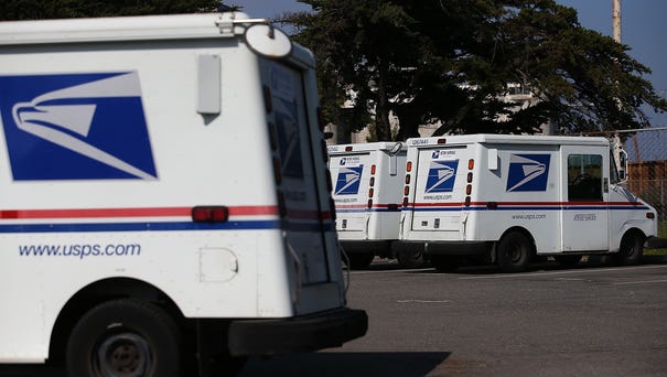 U.S. Postal Service mail vehicles sit in a...
