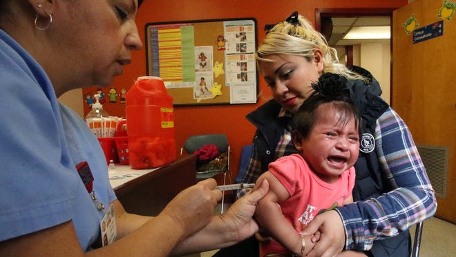 Maria Lourdes Ramos, a medical assistant at the Henderson Clinic at 721 S. Mesa St., administers a measles, mumps and rubella vaccine to 1-year-old Danna Sofia Torres with help from her mother, Ana Karin Solis. The toddler received a variety of vaccines on both legs and her right arm. Her mother said the vaccines are important for the health of her daughter because "they prevent sicknesses."