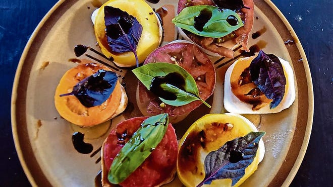 A mix of purple and green basil and a balsamic reduction atop pieces of caprese and different colored tomatoes makes a more colorful plate.