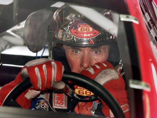 Darrell Waltrip sits in his race car during a break