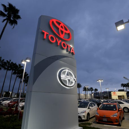 A Toyota dealership signs glows over a car lot in Tustin Calif.