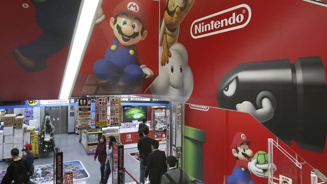 In this Nov. 15, 31, 2018, file photo, shoppers standing on an escalator passes by the logo of Nintendo at an electronics store in Tokyo.