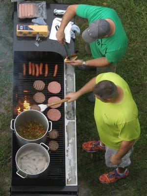 Neal Klein, front, and Todd McDonald grill hamburgers, hot dogs and bratwursts to be sold at the concession stand at Fort Myers High School during their first game of the season against Cape Coral High School.