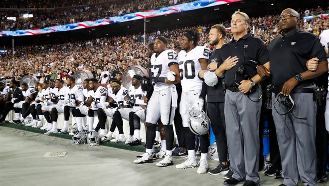 Some members of the Oakland Raiders sit on the bench during the national anthem Sunday, with former CSU linebacker Cory James (57) standing with arms linked with a teammate.