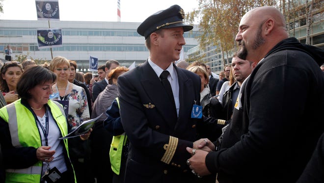 A pilot shakes hands with an Air France worker as they gather in front of the company headquarters to demonstrate against the pilots strike, in Roissy, outside Paris, Wednesday, Sept. 24, 2014.